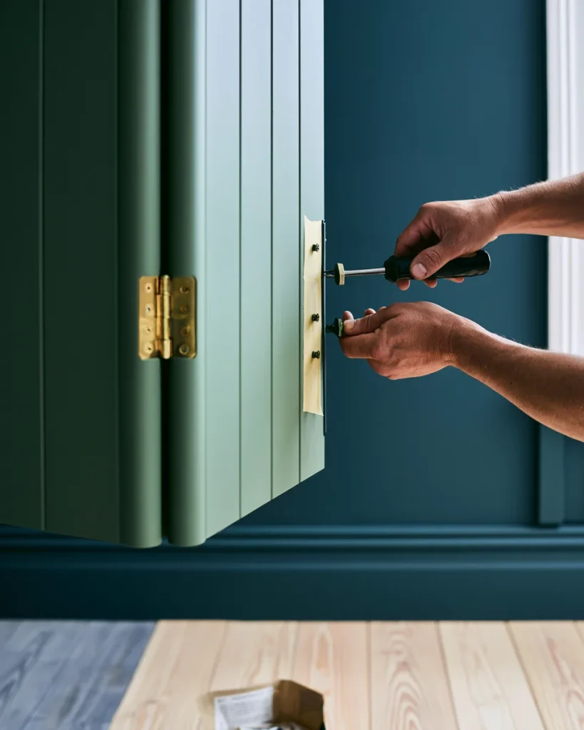 Hands unscrewing a bi-fold closet door hinge, with the screws taped to the track beside them so the change stays reversible for a rental.